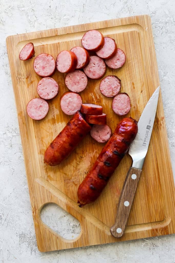 Sliced sausage on a wooden cutting board with a knife.