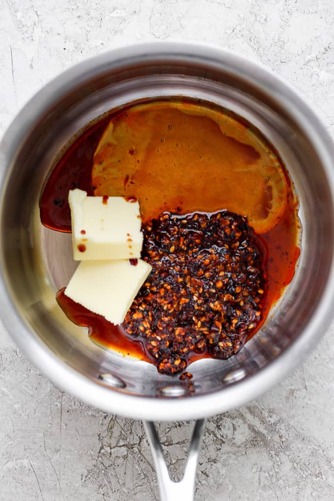 Ingredients in a saucepan including butter, chili flakes, and a dark liquid, possibly soy sauce or vinegar, preparing for a recipe.