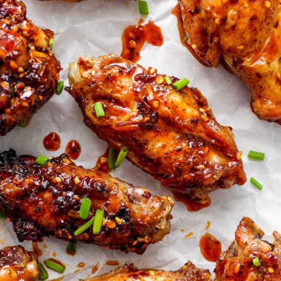 Glazed chicken wings on parchment paper garnished with sesame seeds and chopped green onions.