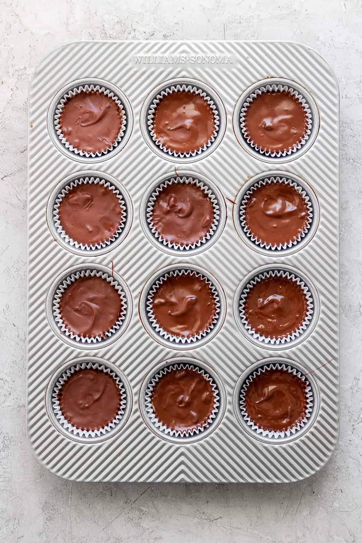 A tray of freshly baked chocolate muffins in paper liners, organized in a 4x3 grid, on a white textured surface.