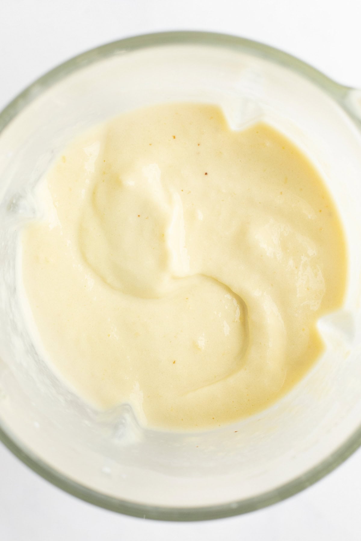 A close-up of a bowl containing smooth, creamy, beige-colored sauce or dressing.