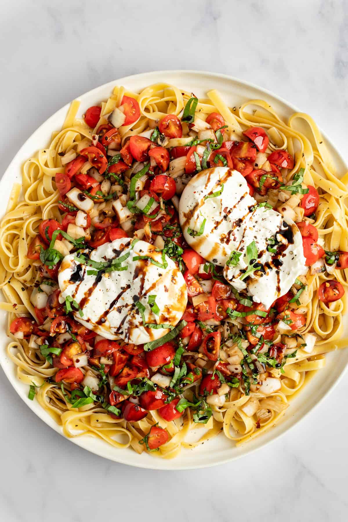 A plate of pasta topped with two poached eggs, cherry tomatoes, herbs, and a drizzle of balsamic glaze.