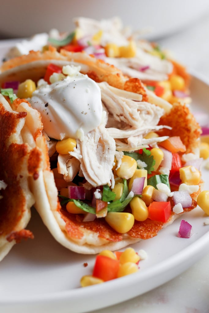 Plate with chicken tacos garnished with corn, diced tomatoes, onions, fresh cilantro, and a dollop of sour cream.