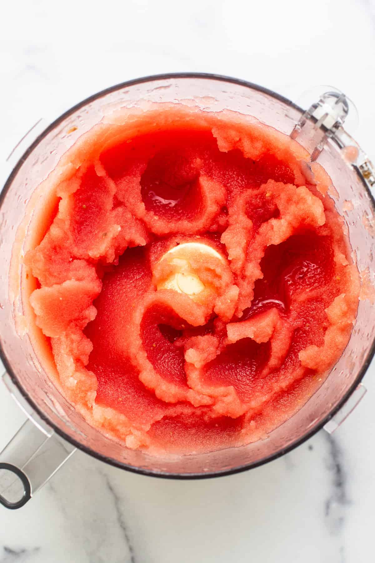 Top view of a blender filled with blended watermelon, showcasing a vivid red mixture with a swirling texture.