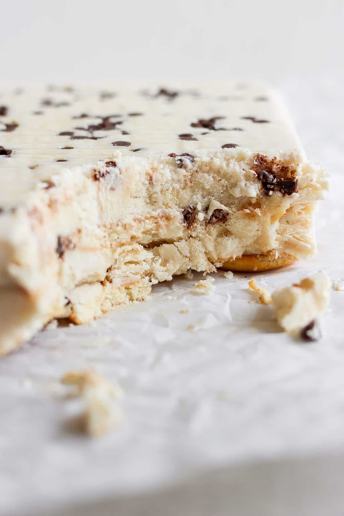 A partially eaten ice cream cake with chocolate chips and a hint of peanut butter banana lies on white parchment paper.