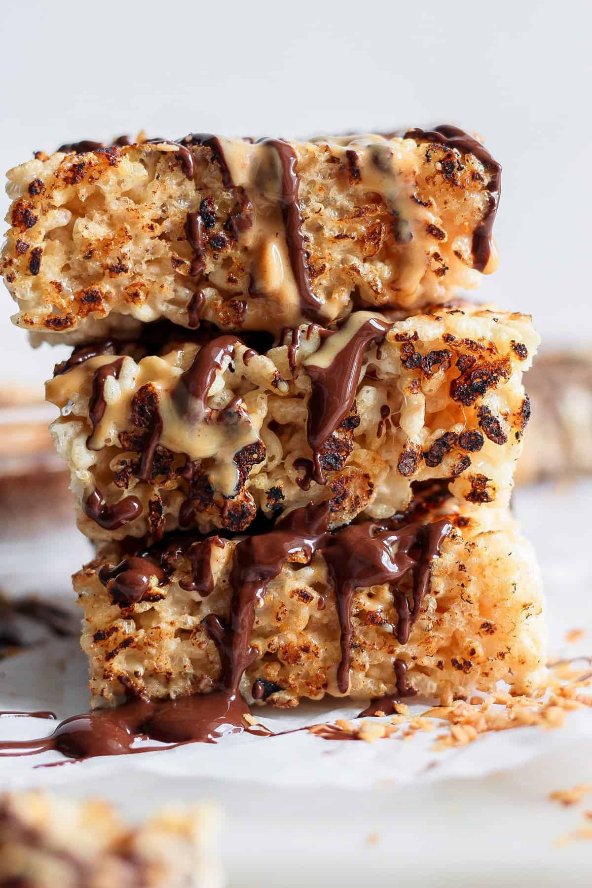 Stack of three toasted rice Krispie treats drizzled with chocolate and peanut butter on a white surface.