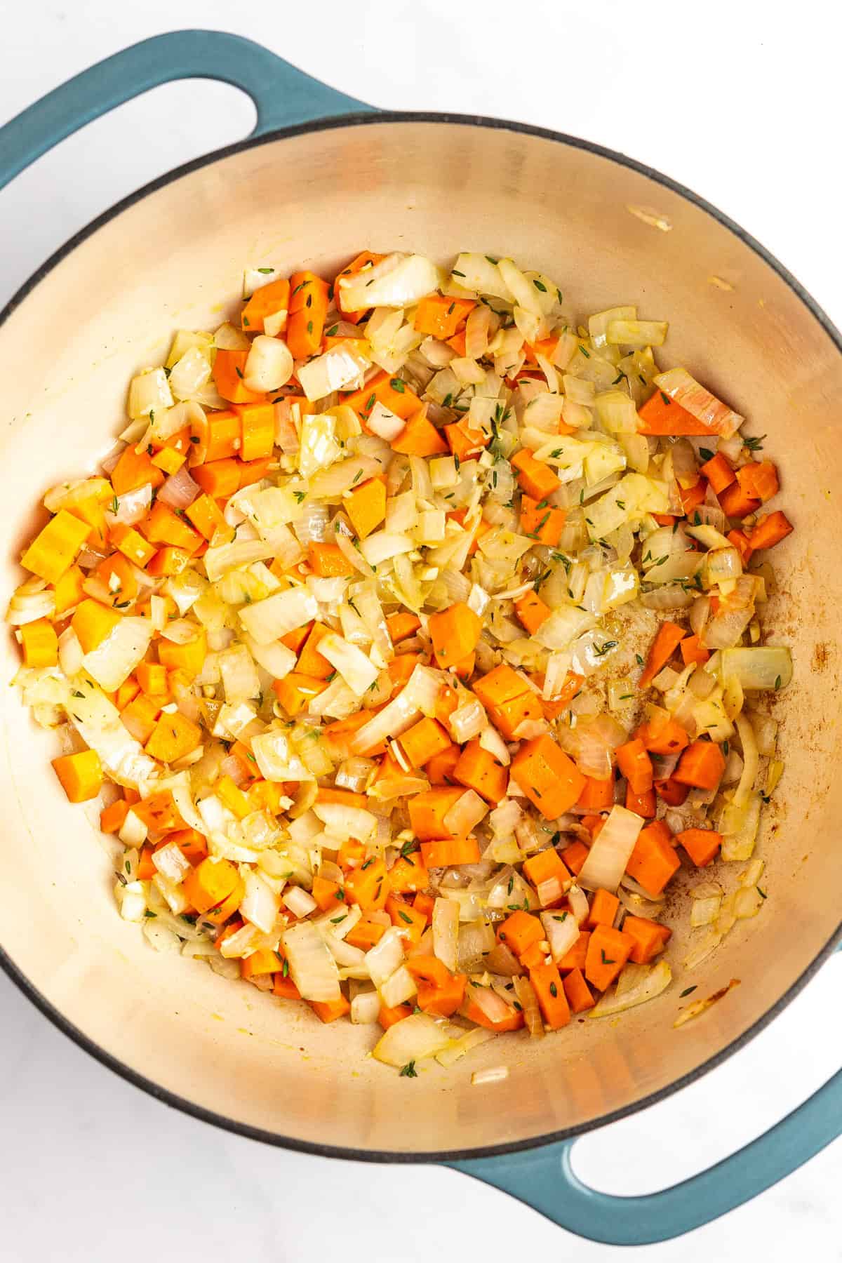 A pot containing sautéed diced onions and carrots.