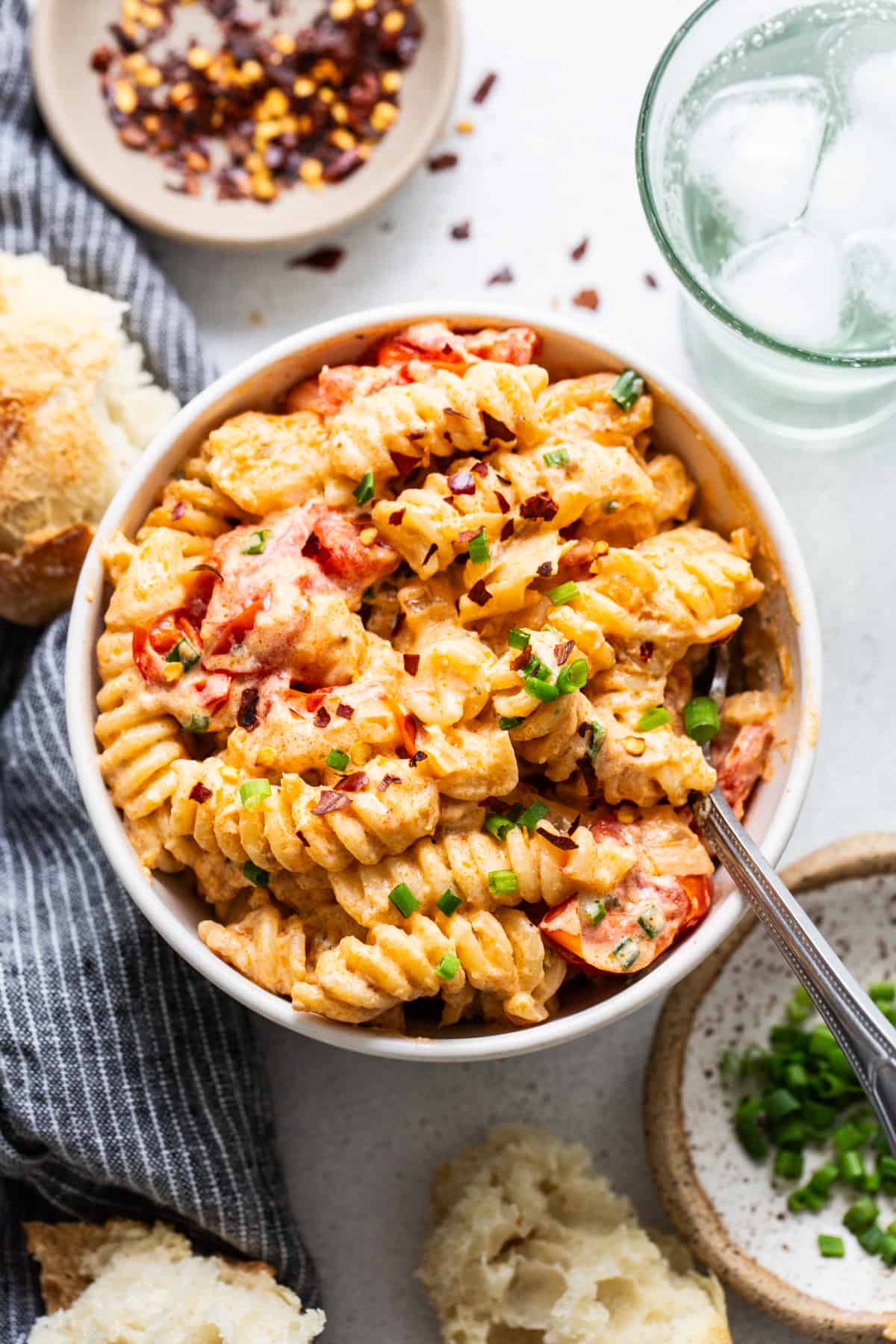 A bowl of creamy tomato pasta garnished with green onions, served with bread and a glass of water on the side.