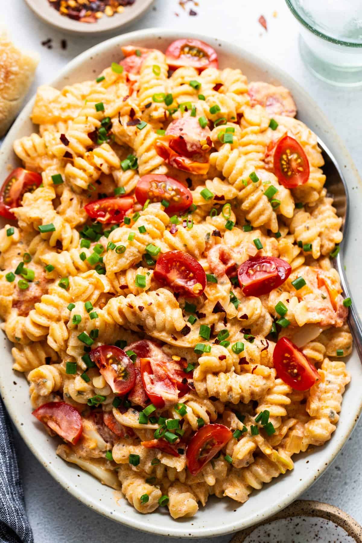 A plate of creamy pasta salad with sliced cherry tomatoes and chopped green onions.