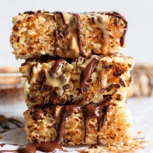 Stacked toasted rice krispie treats drizzled with chocolate and caramel sauces on a white surface.