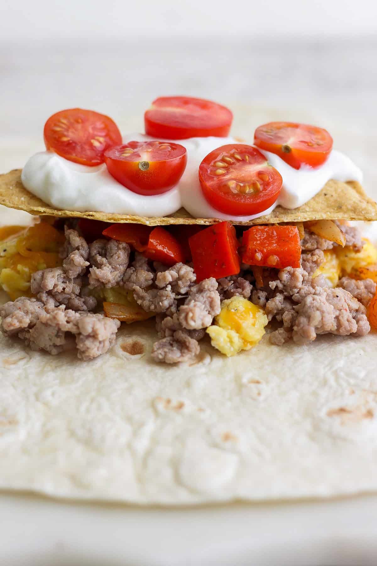 Taco with ground meat, diced red peppers, pineapple, and cherry tomatoes, topped with sour cream.