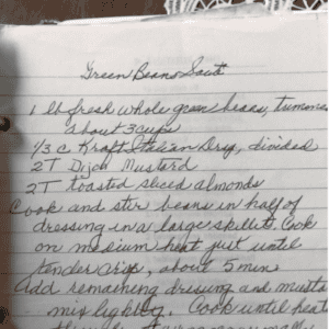 Handwritten recipe for a green bean saute salad on lined paper, featuring fresh green beans, Italian dressing, Dijon mustard, and toasted sliced almonds. The easy-to-follow instructions guide you through creating this crisp and flavorful dish.