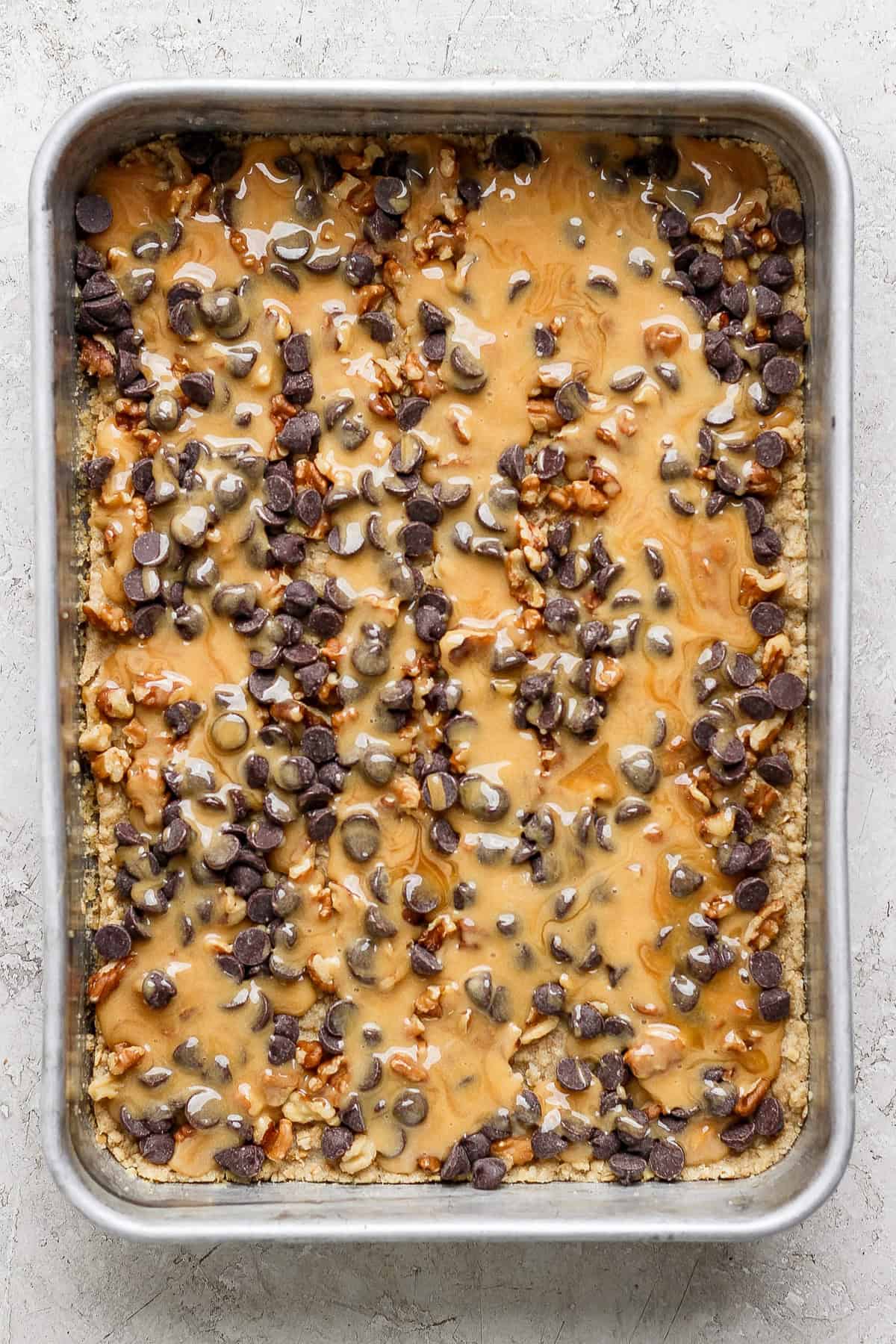 A baking tray filled with a dessert topped with melted caramel, chocolate chips, and chopped nuts.