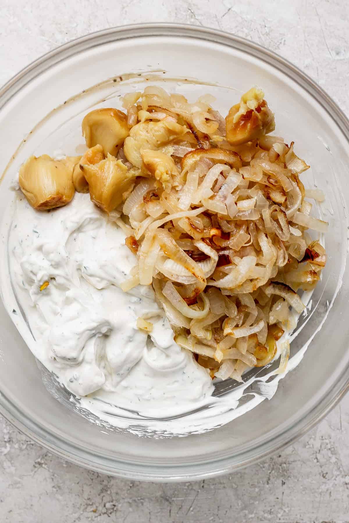 A bowl contains roasted garlic, caramelized onions, and herb-infused creamy dip.