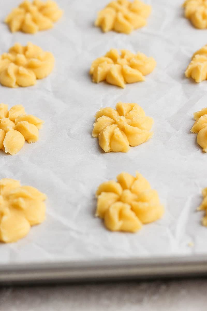 Raw cookie dough shaped into floral patterns on a parchment-lined baking sheet.