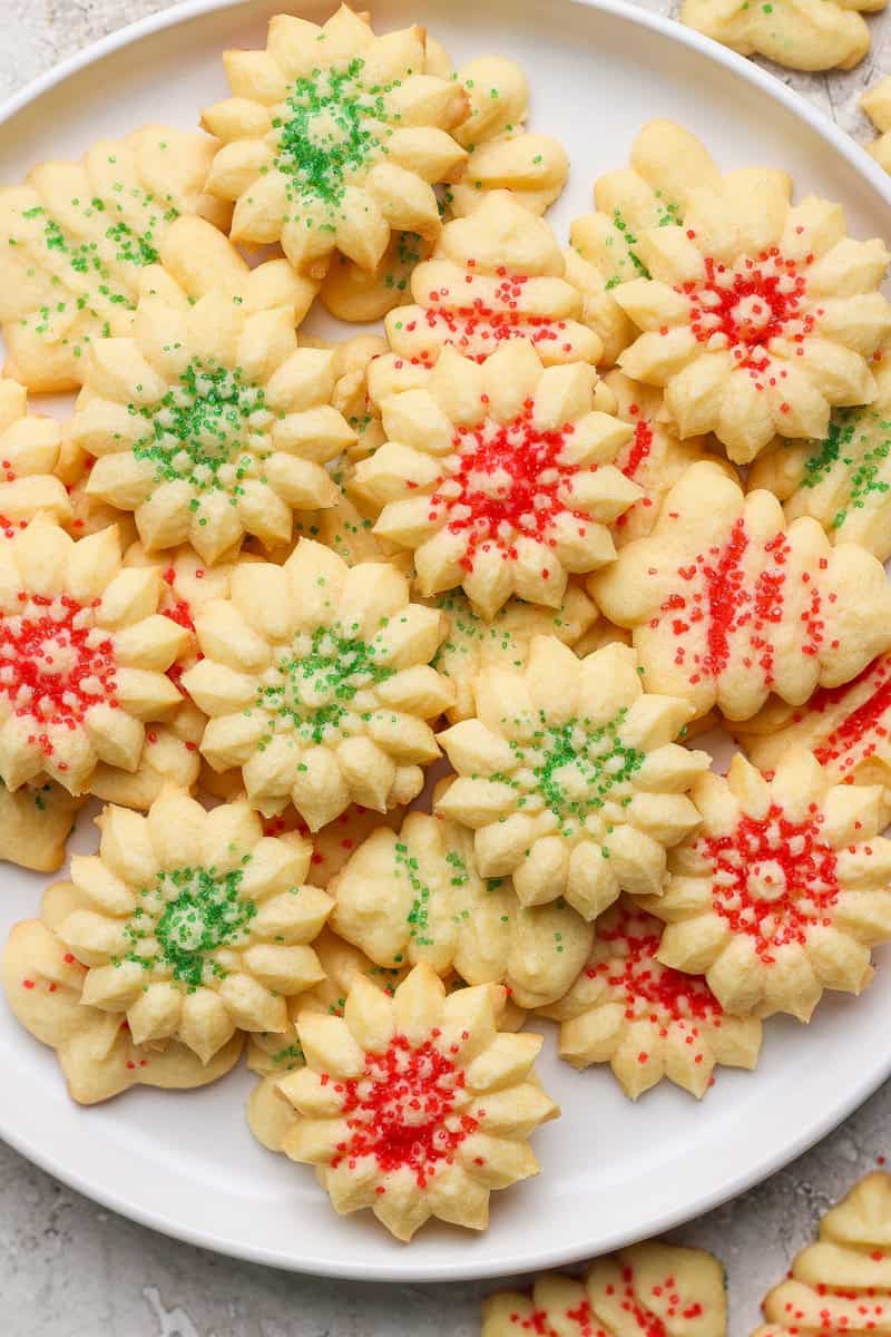 A white plate filled with flower-shaped cookies topped with red and green sprinkles.