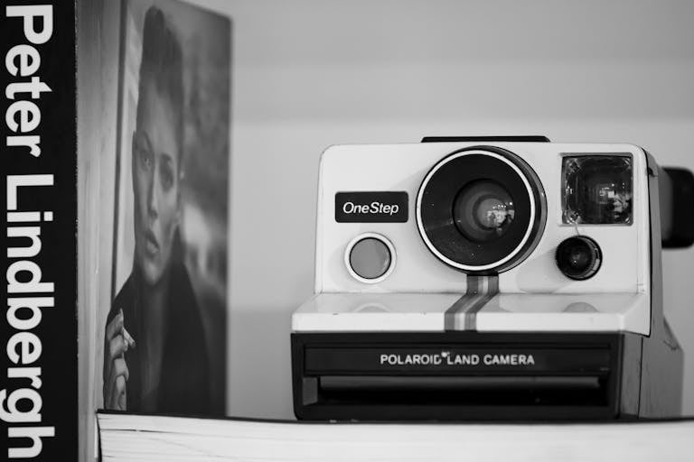 Black and white photo of a Polaroid camera and photography book, artistic composition.