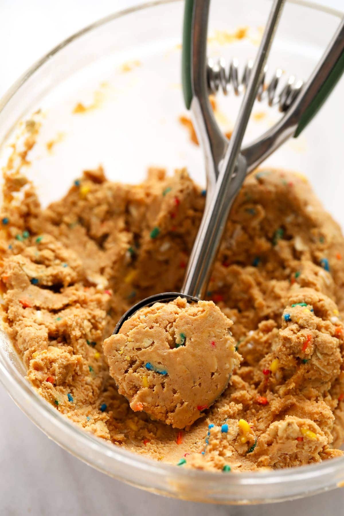 These super flavorful Cake Batter Protein Balls are energy packed from 6 simple ingredients. And no food processor required! cake batter protein ball dough in a bowl being scooped into balls