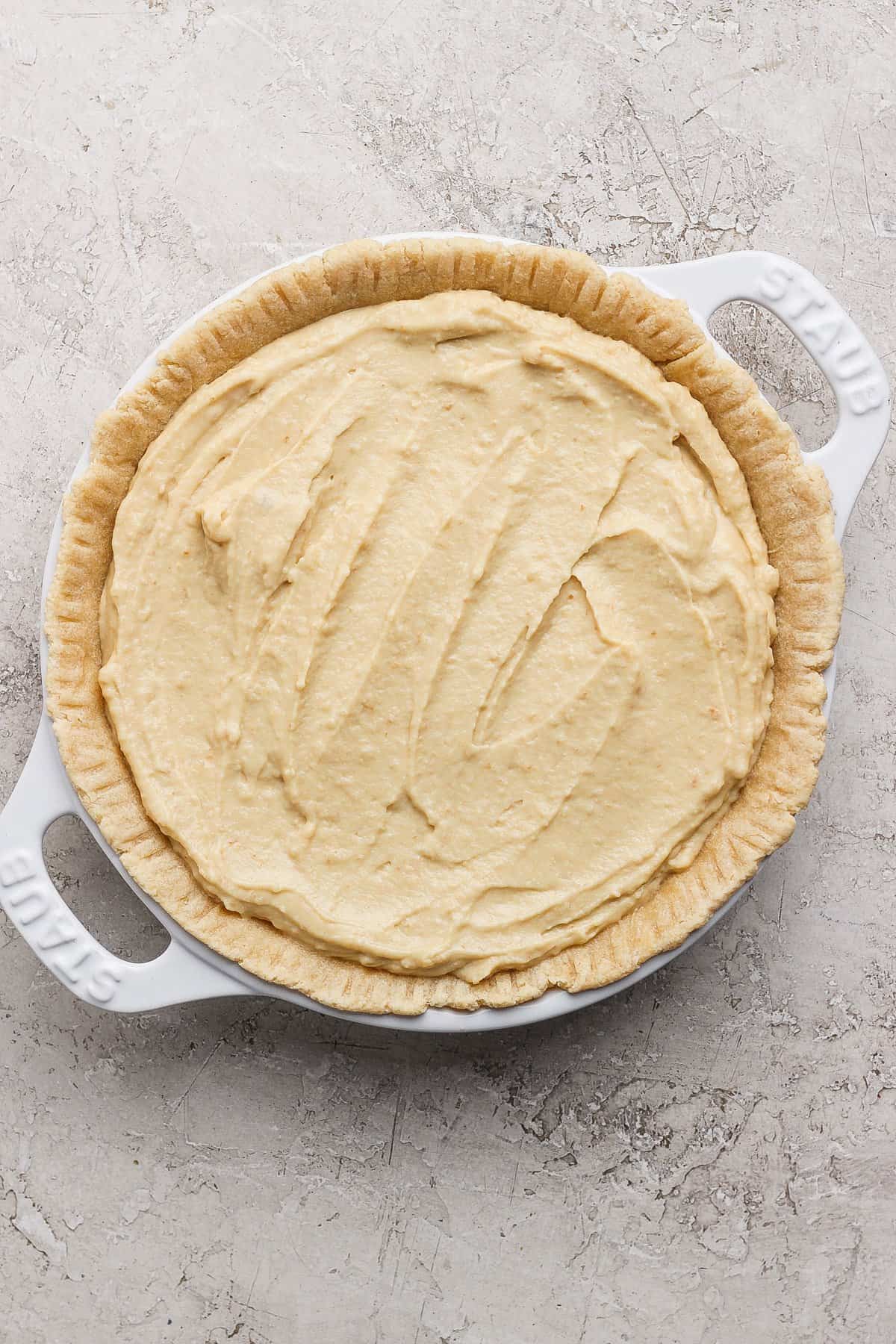 Unbaked pie crust filled with creamy batter in a white baking dish on a textured surface.