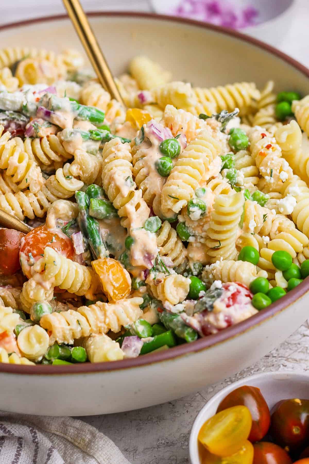 A bowl of rotini pasta salad with peas, asparagus, cherry tomatoes, and a creamy dressing.