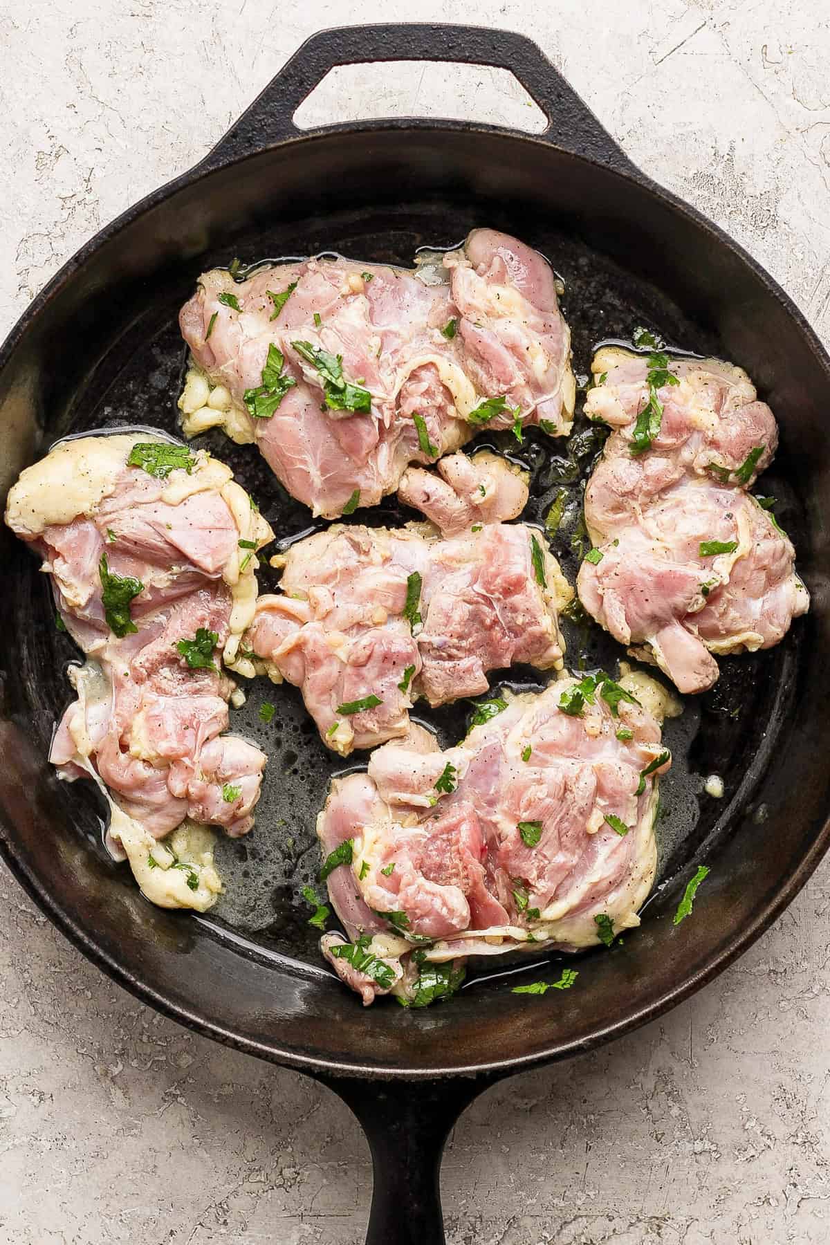 Get your meal prep on with this healthy meal prep cilantro lime chicken served next to a delicious cauliflower rice! This meal prep recipe is low-carb, high-protein, and about to be a staple in your routine. Don't forget to serve the cilantro lime chicken next to homemade cauliflower rice for a complete meal prep meal! Raw marinated chicken pieces with herbs placed in a black cast iron skillet on a light countertop, perfect for easy chicken meal prep.