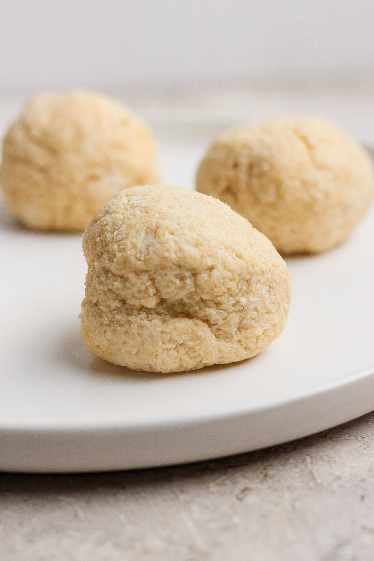 Three round, lightly textured dough balls are arranged on a white plate with a neutral background.