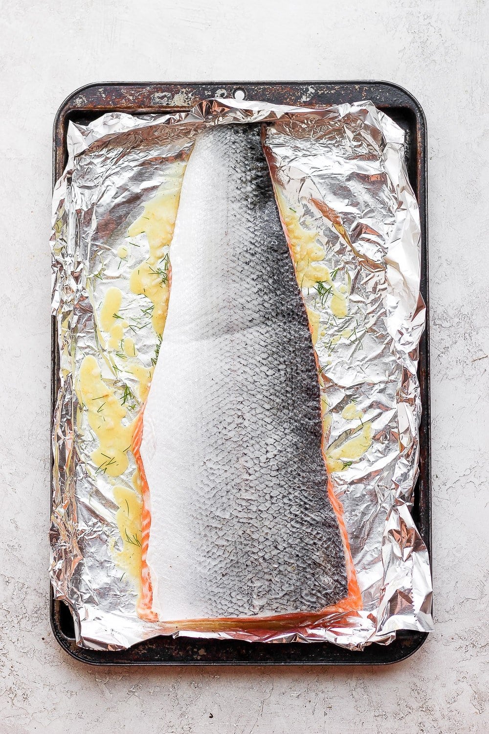 This simple salmon marinade is so fresh and delicious. It's made with fresh lemon, garlic, and dill. You'll never want to eat salmon any other way! Salmon marinating in a baking sheet.