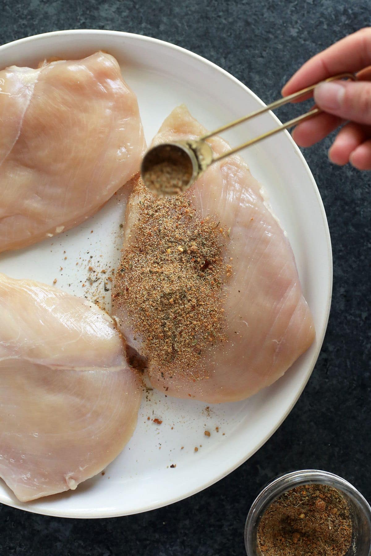 Sprinkling all purpose seasoning on a chicken breast.