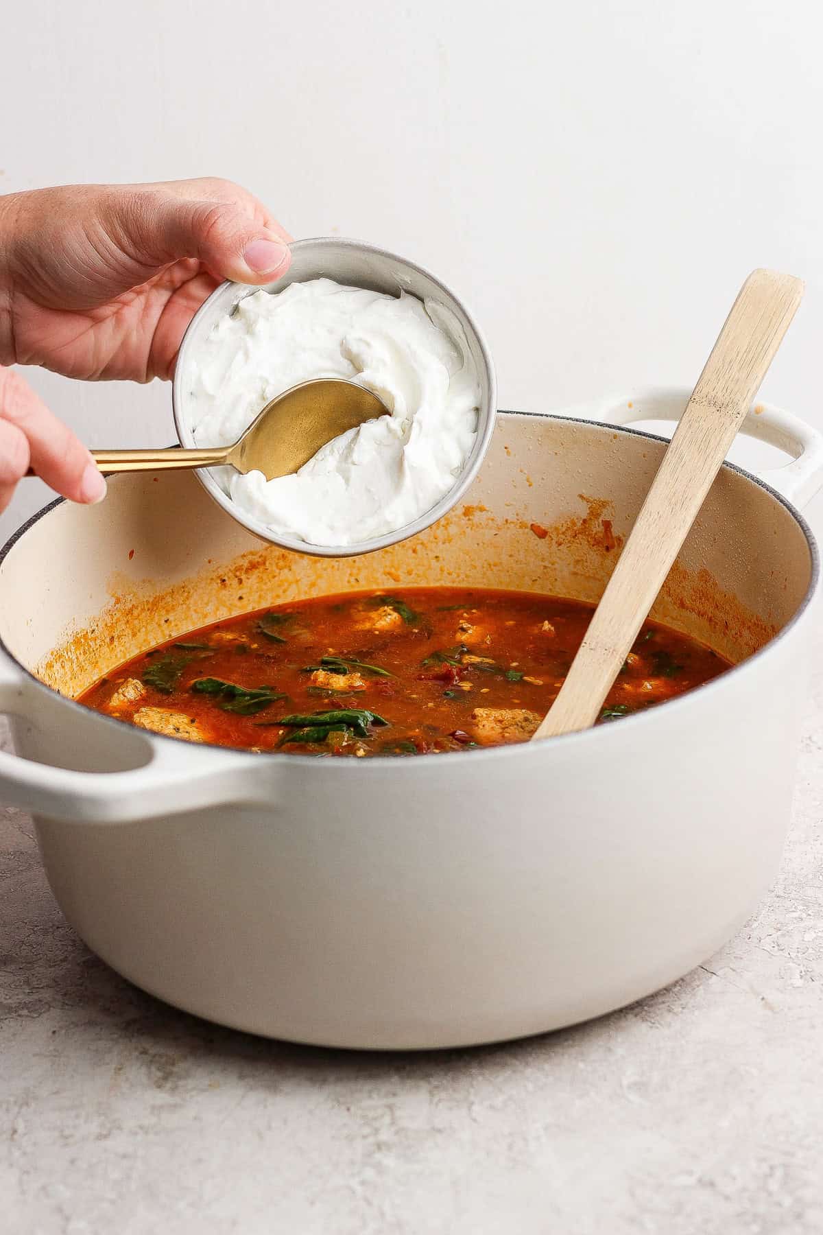 A person pouring cream into a pot of soup.