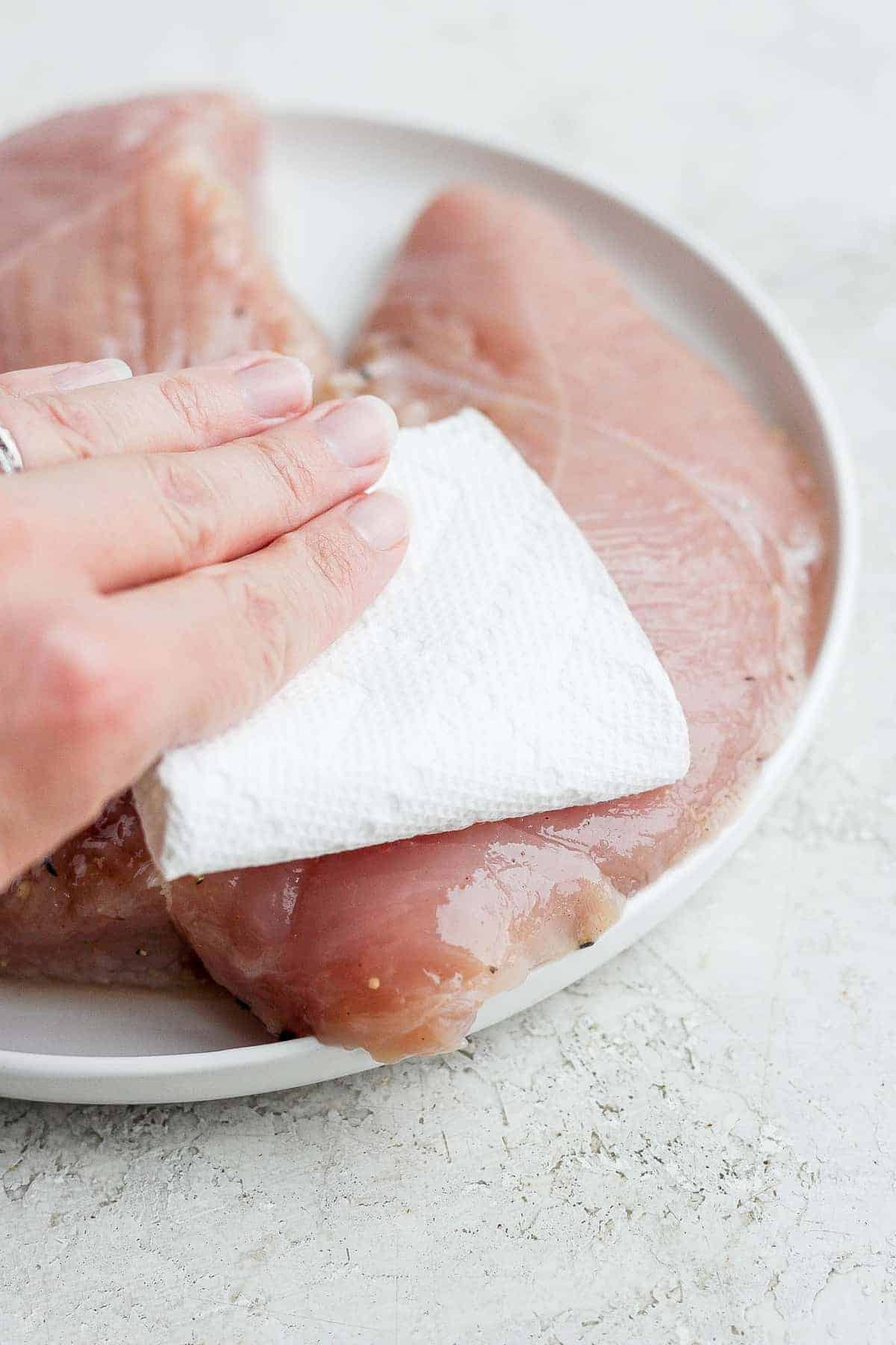 This easy baked turkey tenderloin is made super flavorful with a turkey brine and then our amazing turkey seasoning. Enjoy! hand patting turkey tenderloin on plate.