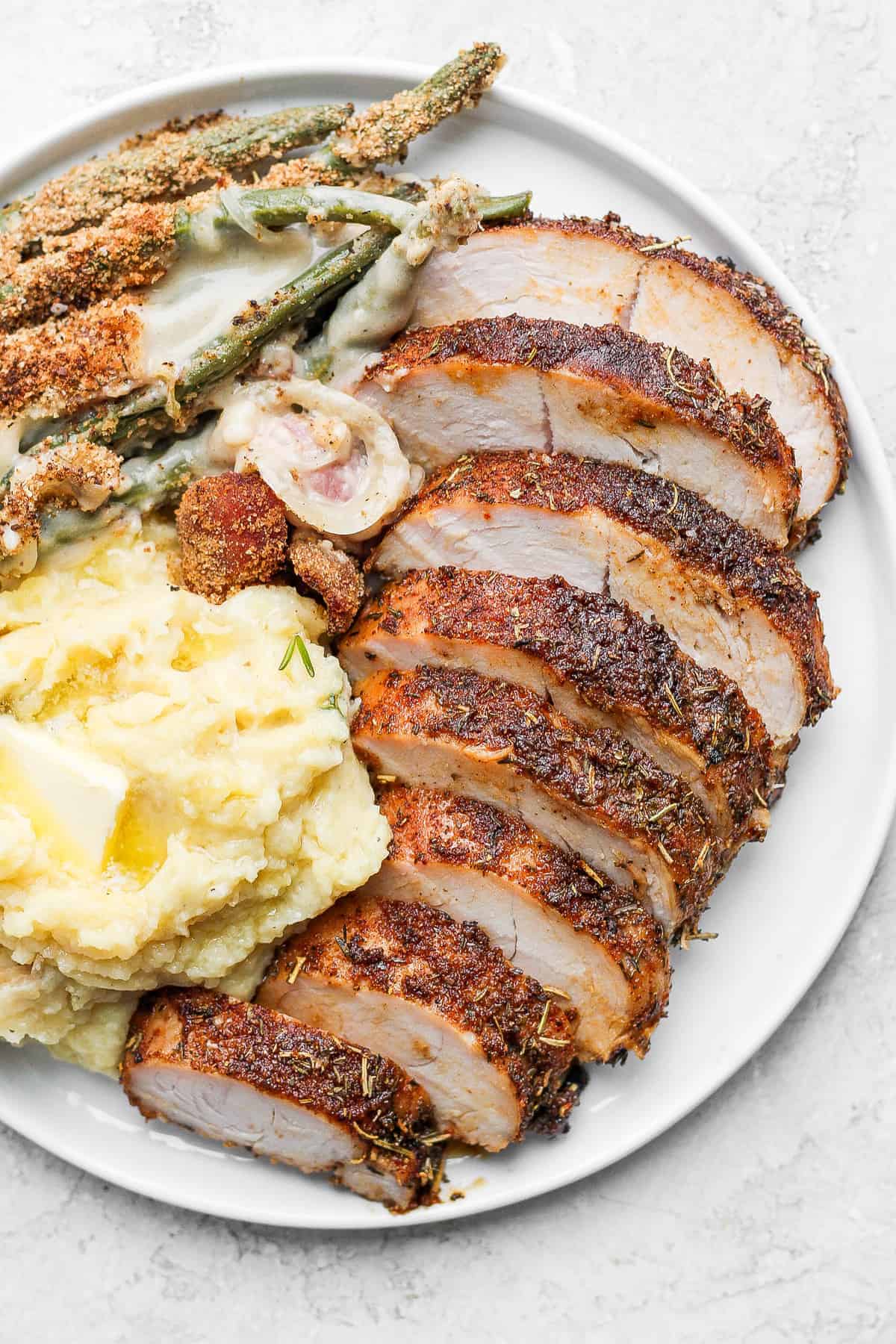 This easy baked turkey tenderloin is made super flavorful with a turkey brine and then our amazing turkey seasoning. Enjoy! sliced turkey tenderloin on plate.