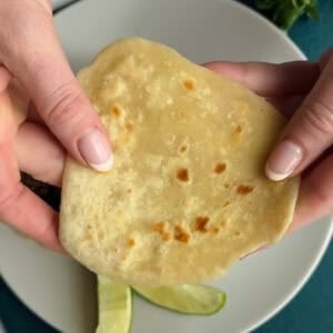 Two hands hold a flatbread over a plate containing lime wedges.