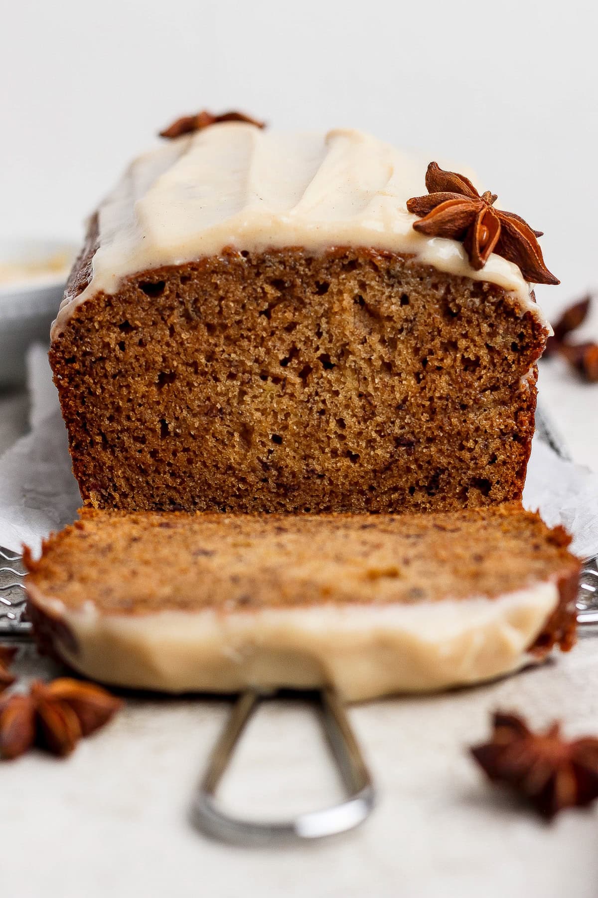 A loaf of spiced banana bread is sliced, topped with a light frosting and star anise decorations placed on and around the bread—a delicious twist on a classic banana bread recipe.