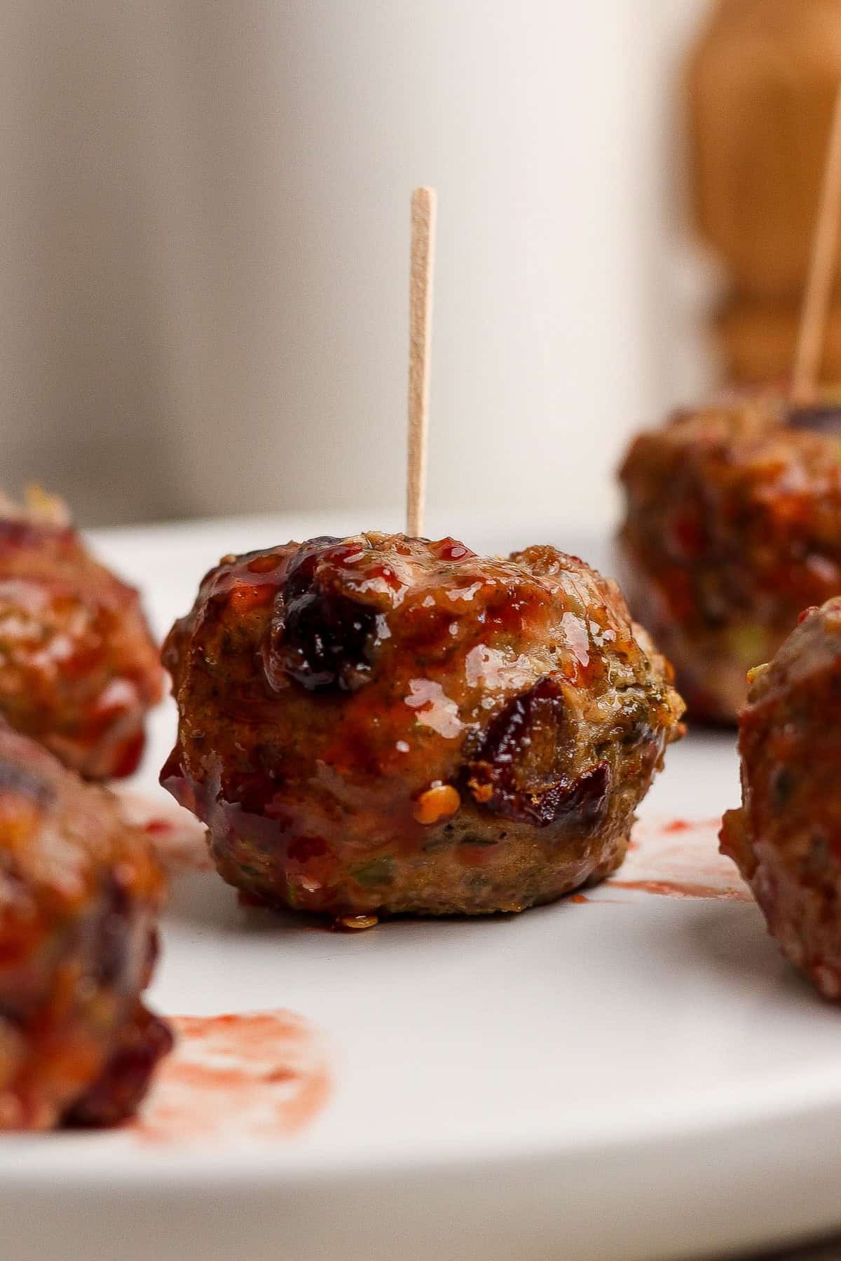 A close-up of glazed meatballs on a white plate, each with a toothpick inserted for serving.