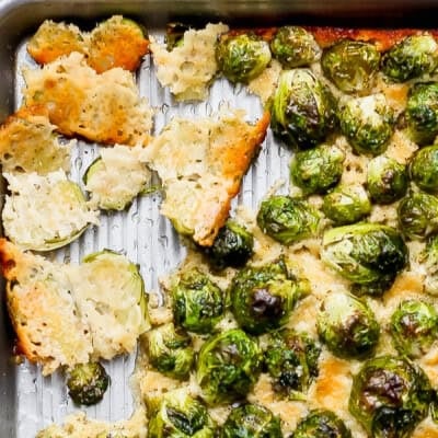 Sheet pan with roasted Brussels sprouts and melted, golden brown cheese, some pieces torn apart from the main section.