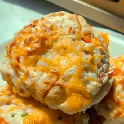 A close-up of cheesy baked biscuits with melted cheddar cheese on top, served on a white plate.