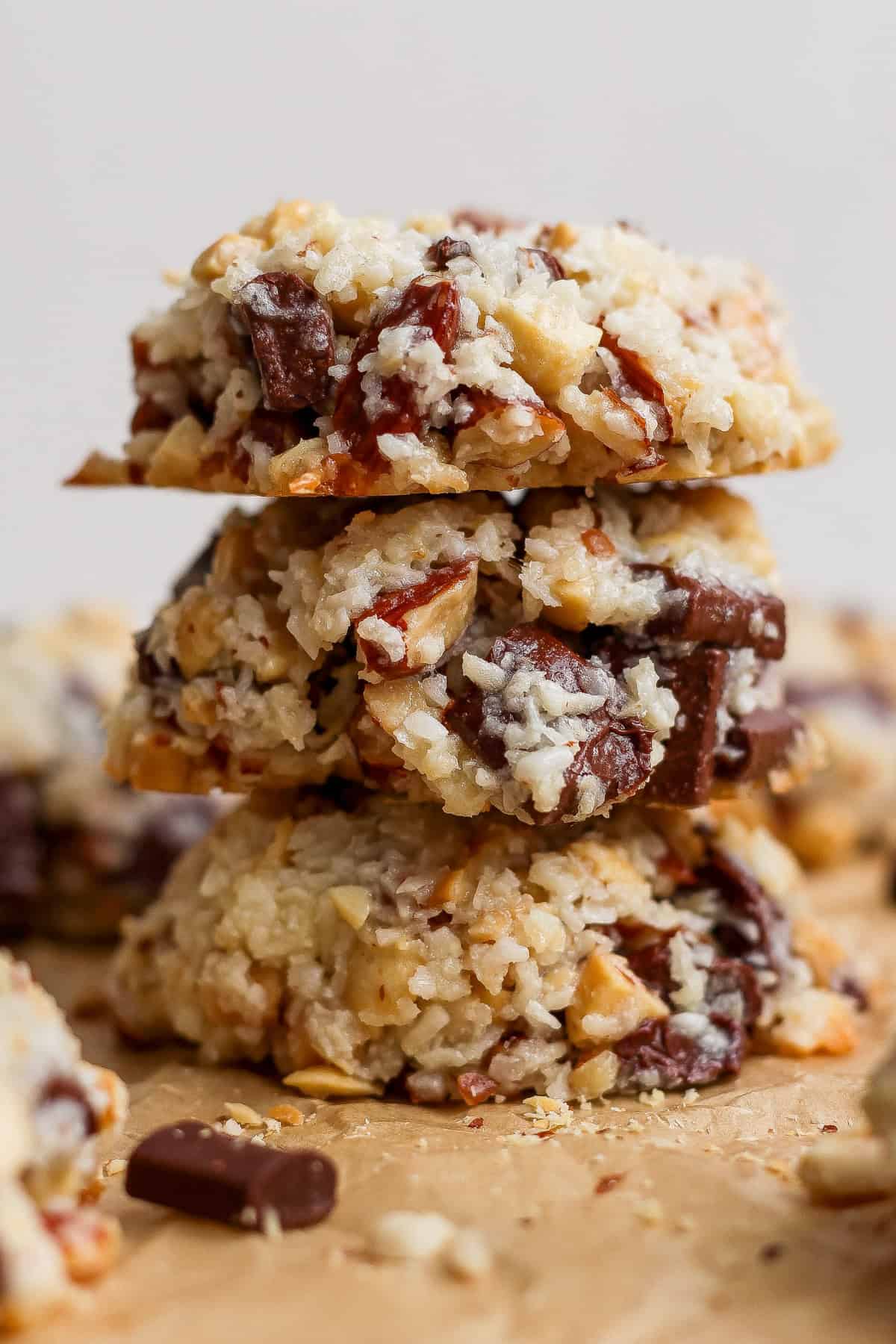 Three coconut, nut, and chocolate chunk cookies are stacked on top of each other on a piece of parchment paper.