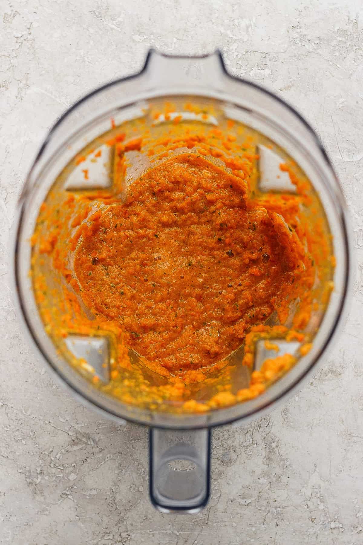 A blender with orange vegetable puree inside, viewed from above on a light-colored surface.