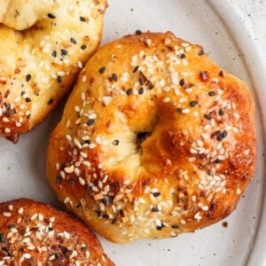Close-up of a bagel topped with sesame and poppy seeds on a white plate.