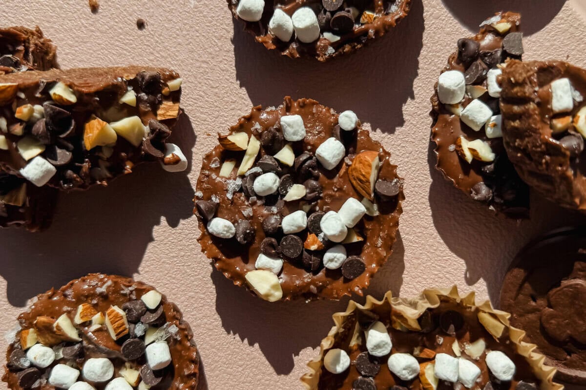Chocolate treats topped with mini marshmallows, chocolate chips, and chopped nuts are arranged on a light textured surface.