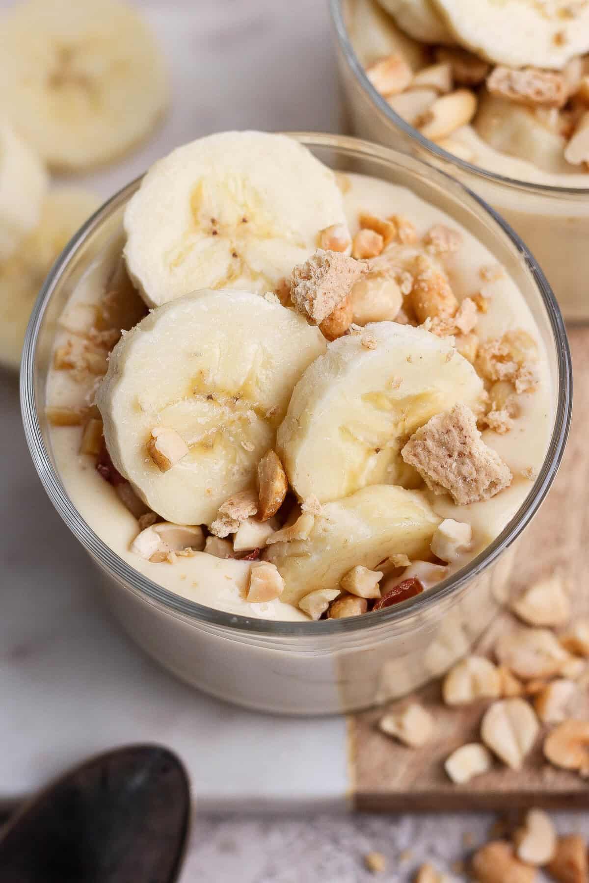 A glass bowl filled with banana pudding, topped with banana slices, chopped nuts, and cookie pieces.