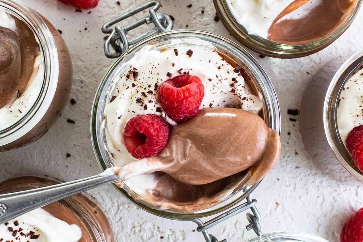 Chocolate mousse in jars with whipped cream and raspberries.