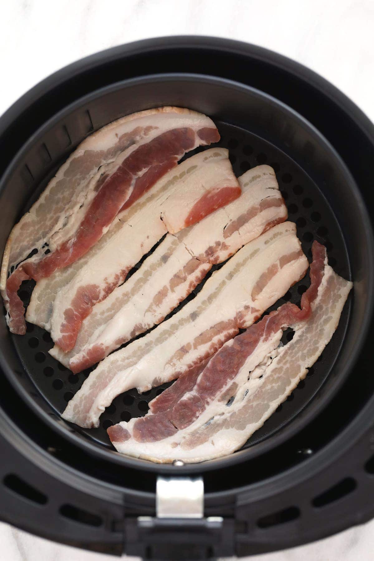 Looking for a quick and easy air fryer bacon tutorial? In this post, we'll teach you how to cook bacon in the air fryer in just a few steps! uncooked bacon in air fryer