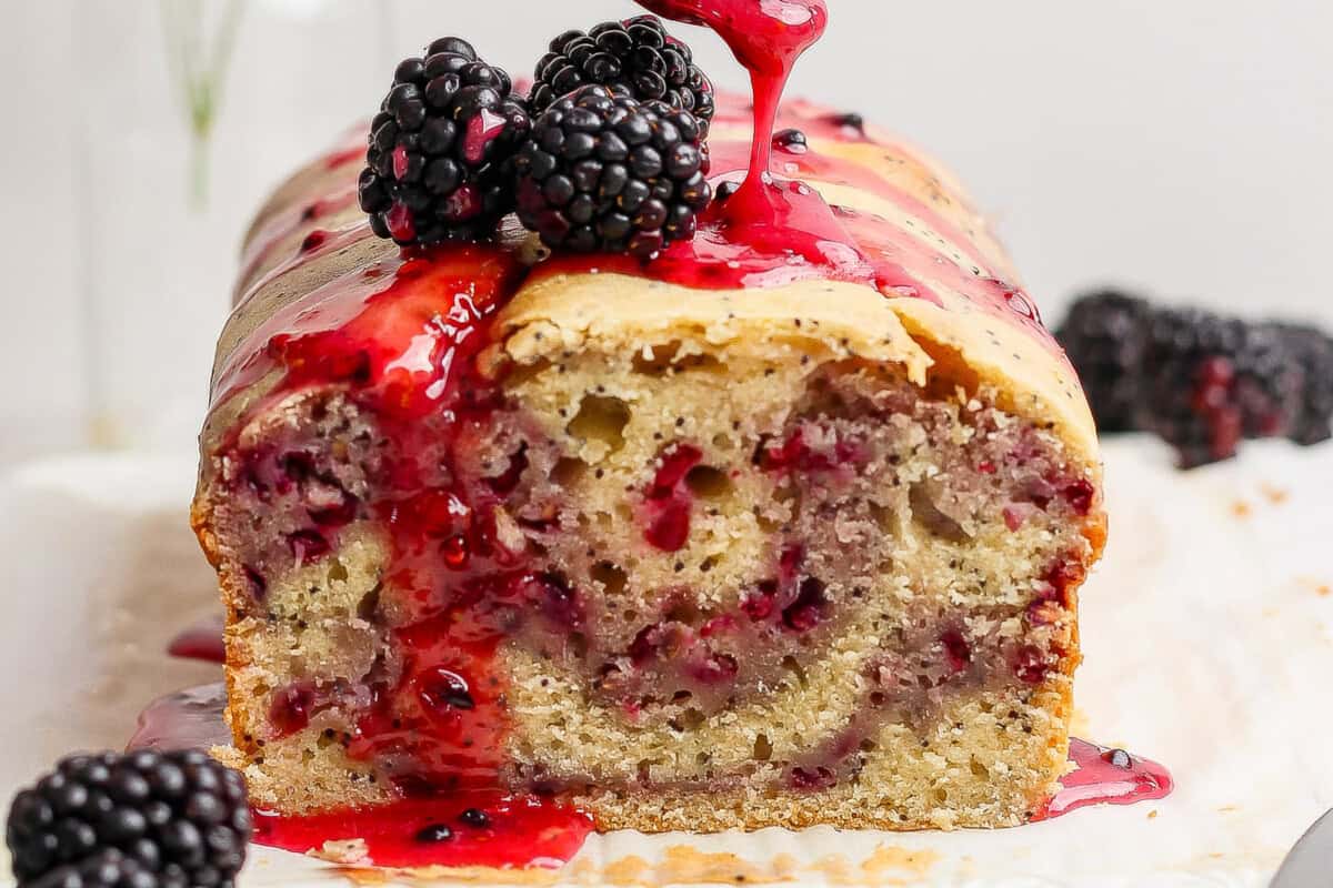 A loaf of blackberry bread topped with blackberries and a drizzle of blackberry sauce.