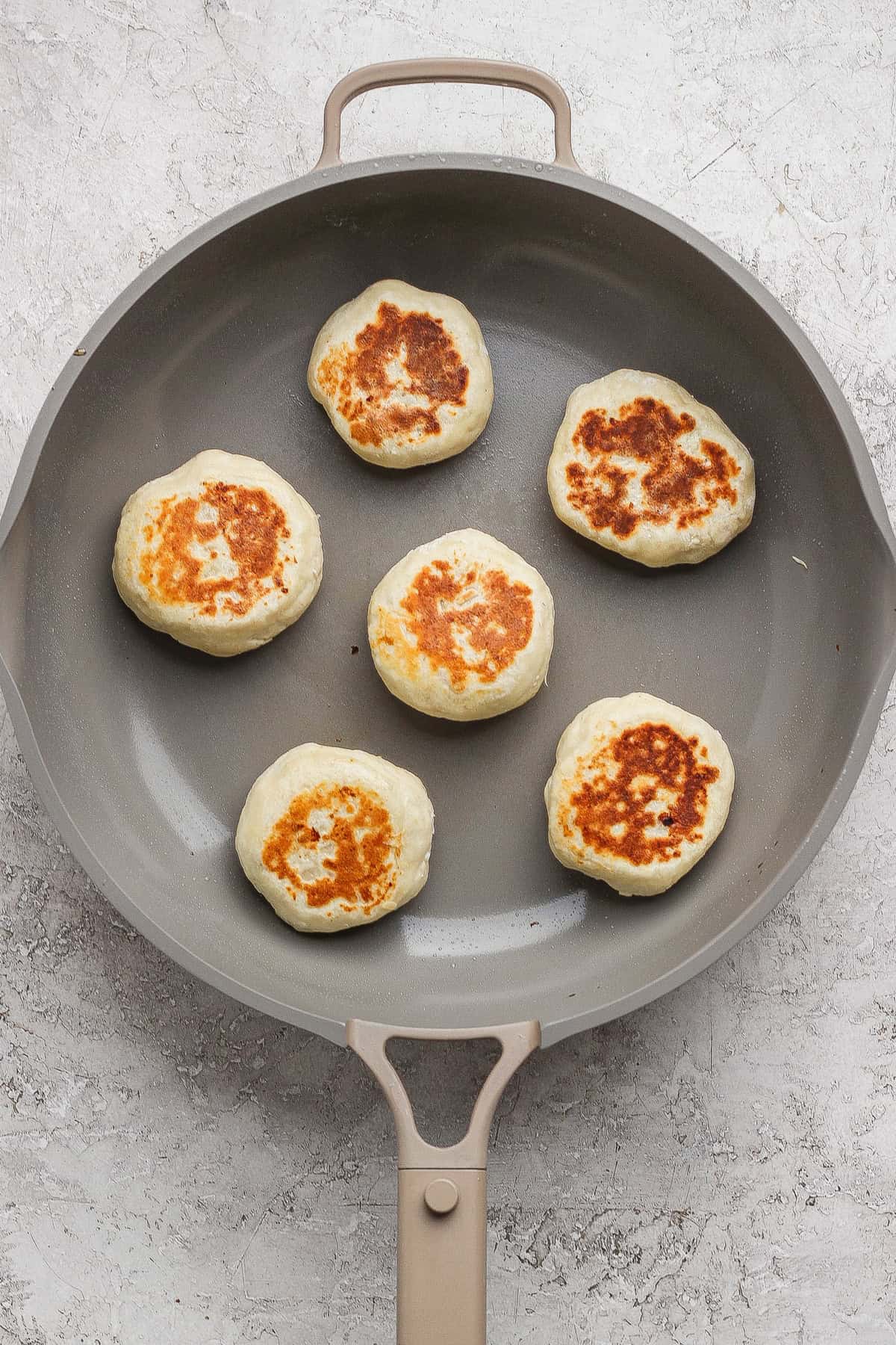 Six round, golden-brown patties are cooking in a nonstick skillet on a light-colored surface.