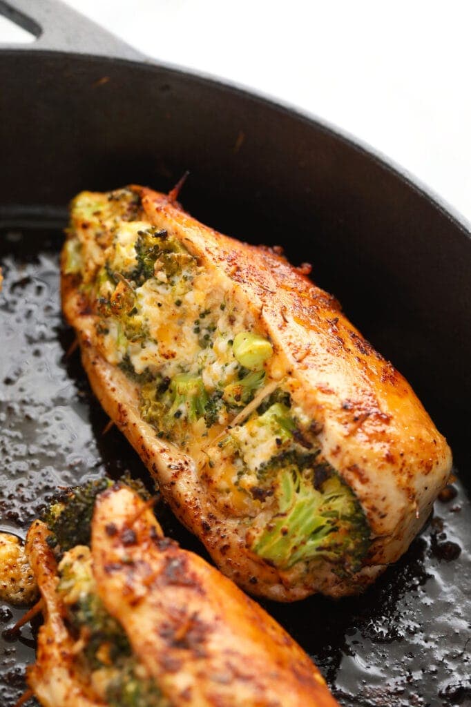 Broccoli and cheese stuffed chicken breast never tasted better! Our super flavorful chicken dry rub and easy broccoli and cheese filling make these stuffed chicken breasts deliciously flavor and protein packed. broccoli and cheese stuffed chicken breasts in a cast iron skillet.