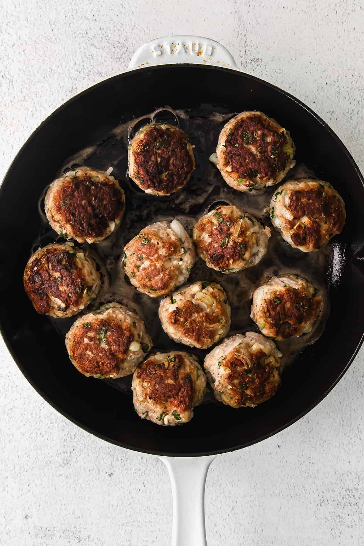 Chicken meatballs in a skillet on a white background.