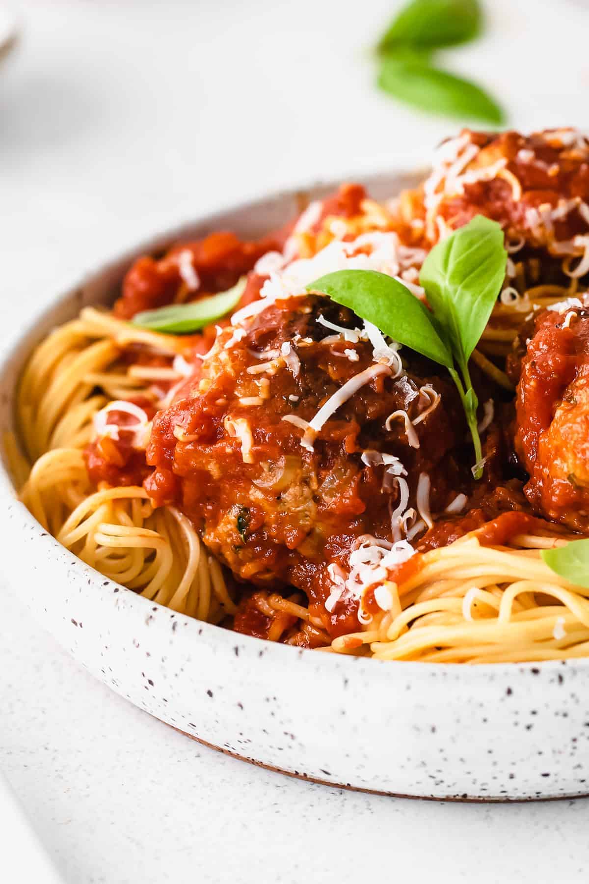 Spaghetti with meatballs and basil on a white plate.