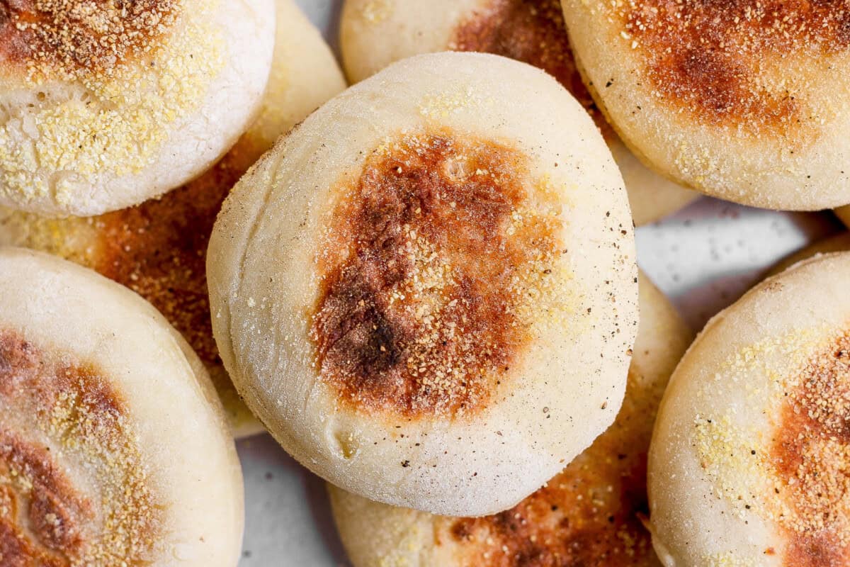 A close-up photo of several golden-brown English muffins sprinkled with cornmeal.
