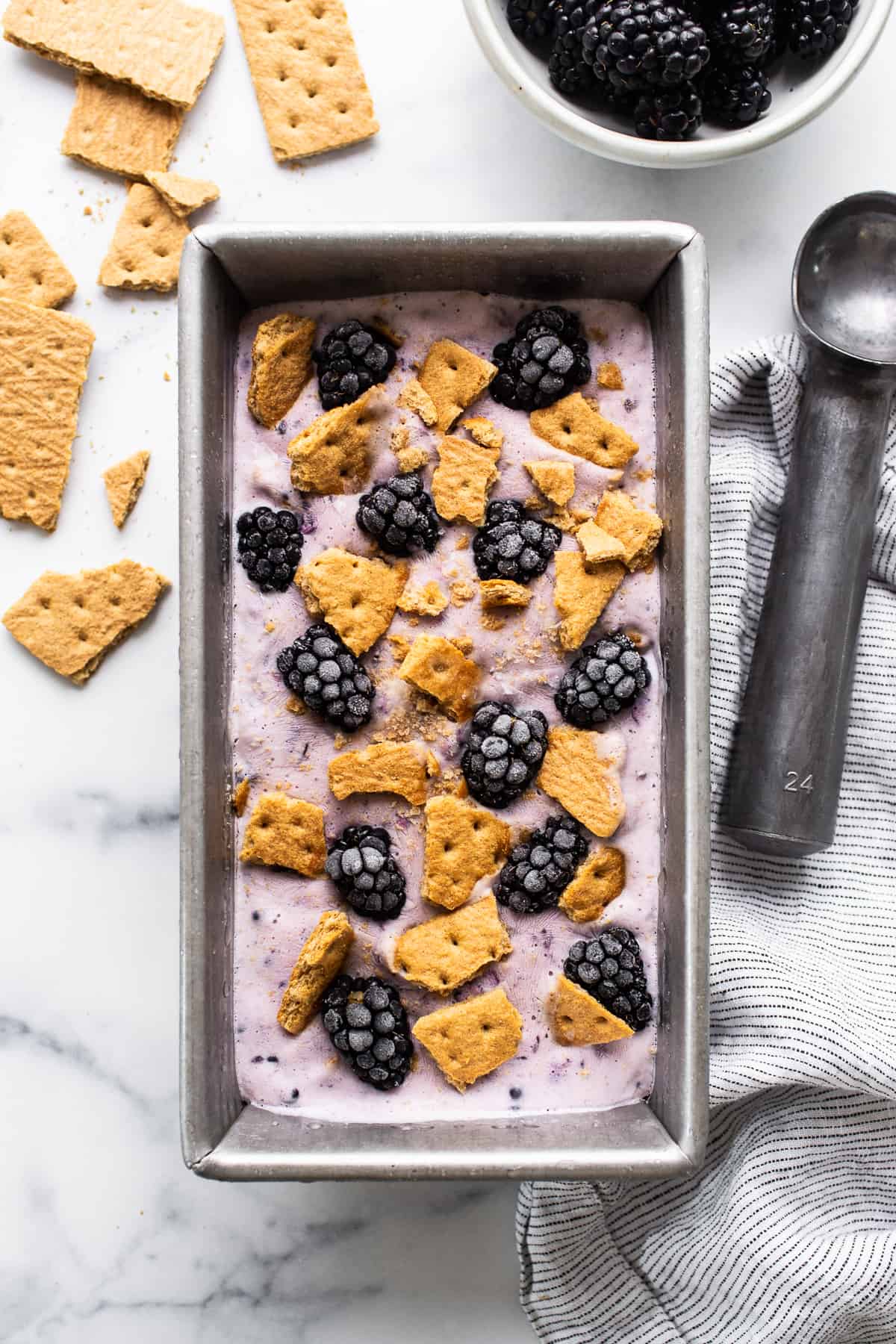 blackberry cheesecake cottage cheese ice cream in a tin loaf pan topped with fresh berries and graham cracker crumbs.
